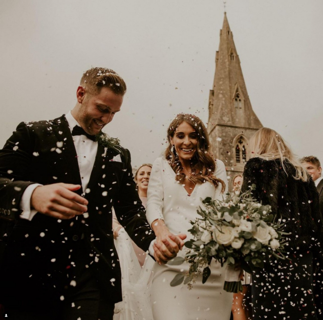 Confetti shot of groom and bride holding a White bridal bouquet for Devon wedding created by Simply Flowers. 