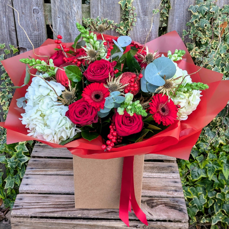 Red and white hand-tied bouquet with roses, hydrangeas, gerberas, eucalyptus and berries, presented in a kraft gift box 